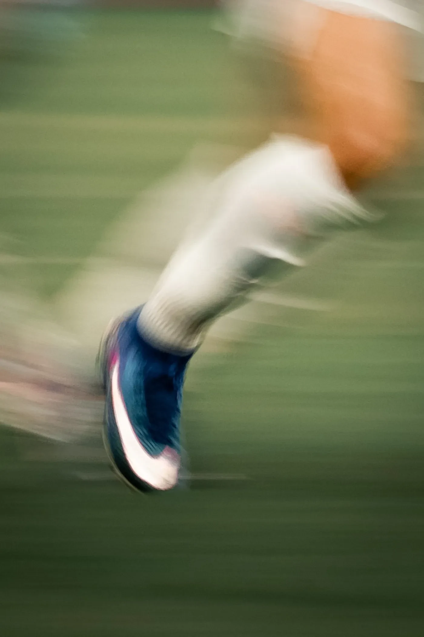 Motion-blurred close-up of a player's boot striking through the grass